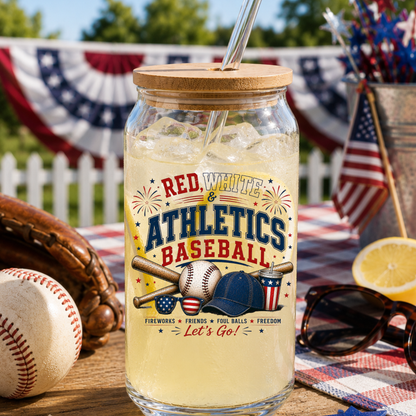 Glass jar with a wooden lid filled with iced beverage, featuring 'Red, White & Athletics Baseball' design, on a table with baseball equipment and American flags.