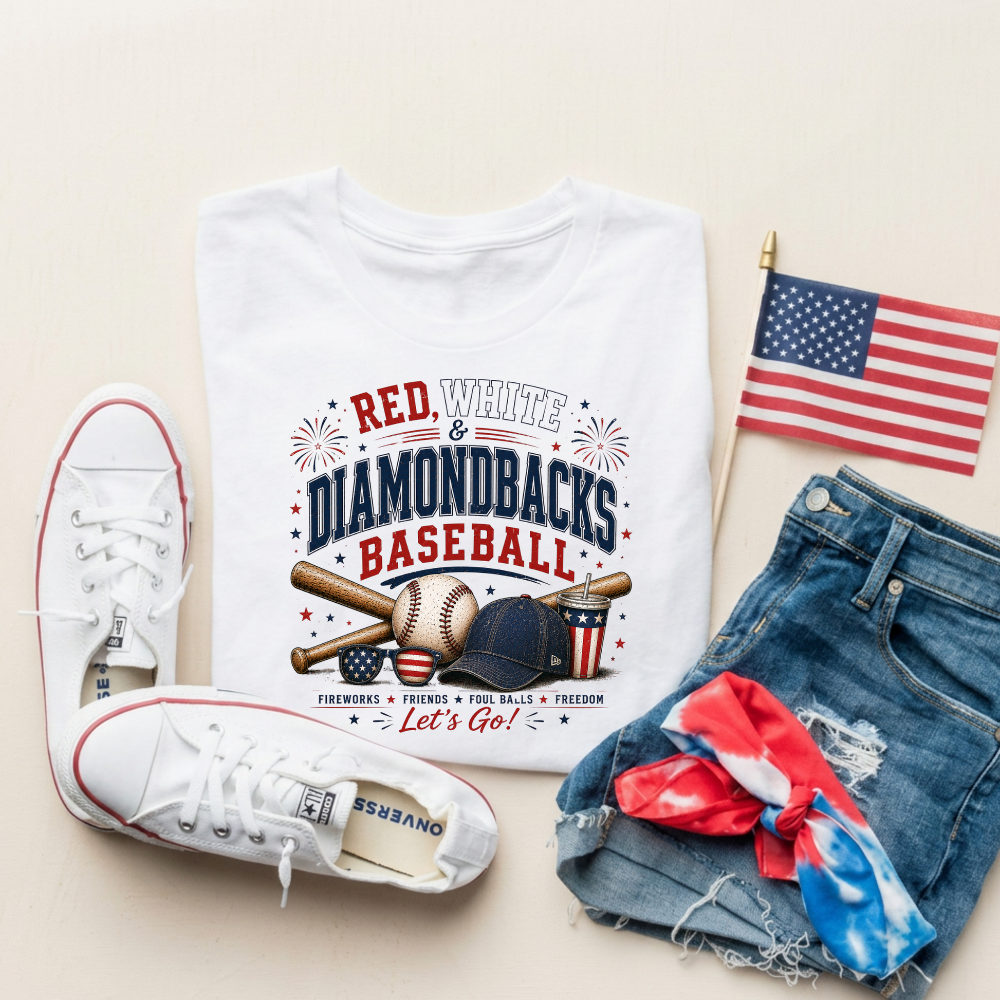 White t-shirt with 'Red, White & Diamondbacks Baseball' design, white sneakers, denim shorts, and American flag on a beige background.