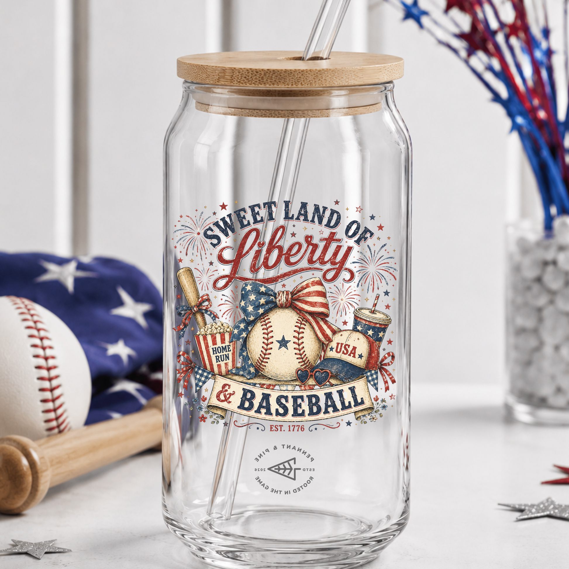 Clear glass tumbler with wooden lid featuring 'Sweet Land of Liberty & Baseball' design, surrounded by American-themed decor.