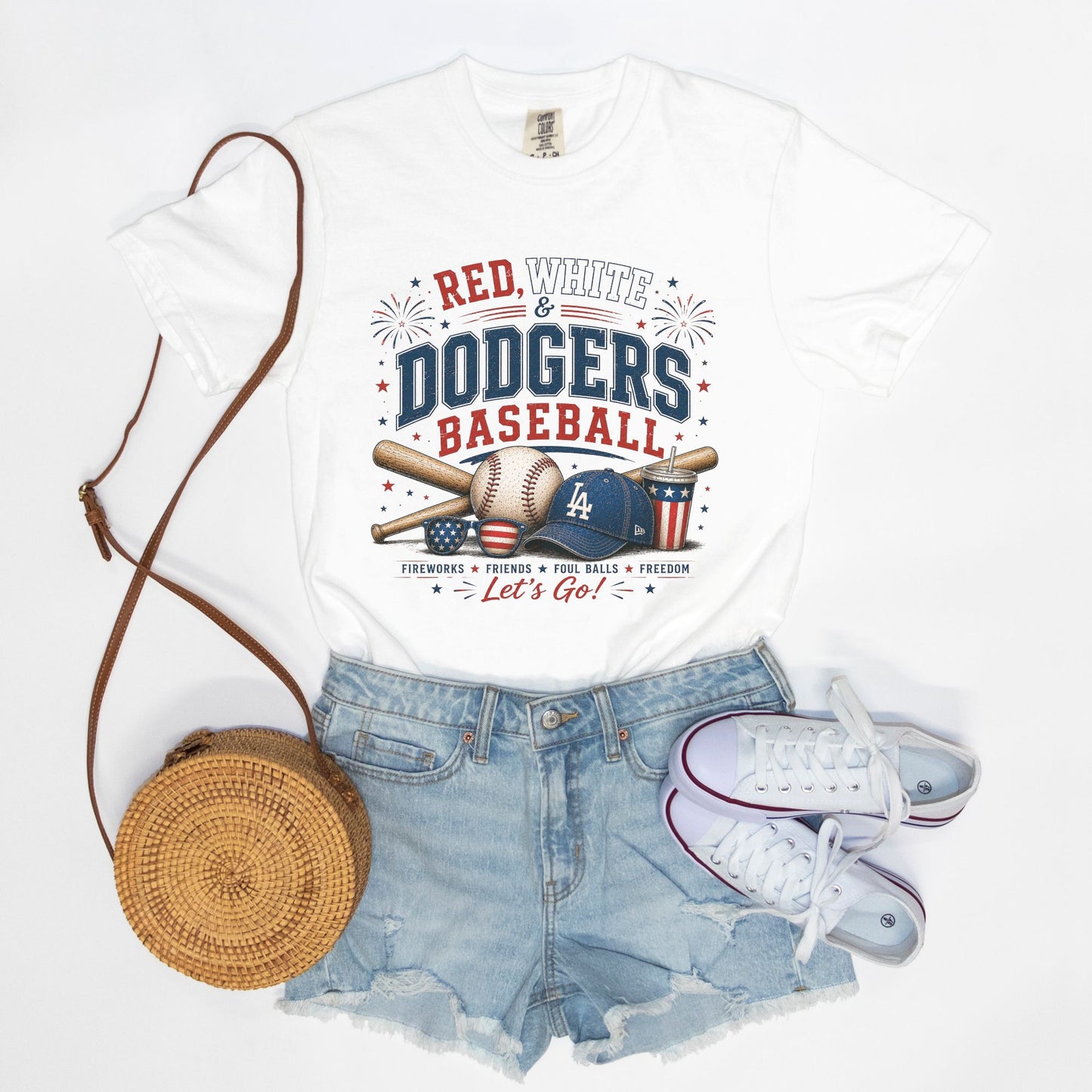 White t-shirt with 'Red, White & Dodgers Baseball' design, denim shorts, white sneakers, and a woven bag on a white background.