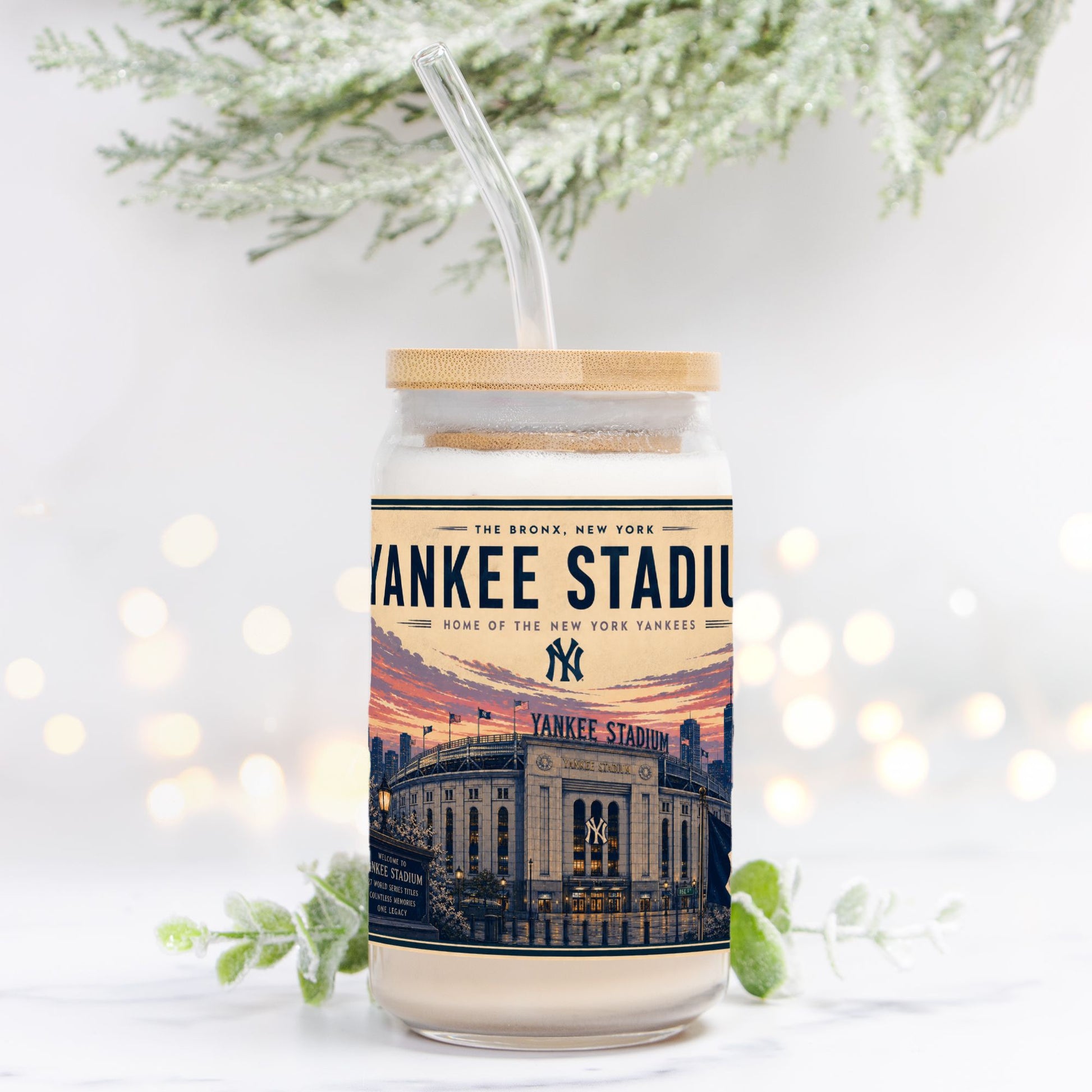 Jar with a lid and straw, featuring a Yankees Stadium design, on a white background with blurred lights and greenery.
