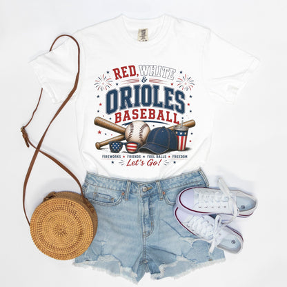 White t-shirt with 'Red, White & Orioles Baseball' design, paired with denim shorts, white sneakers, and a round brown bag on a light gray background.